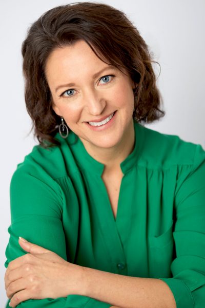 A professional woman in a bright green blouse smiling confidently at the camera with her arms crossed.