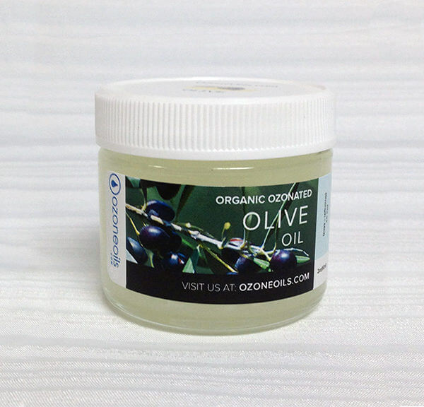 A jar of organic Ozone oil on a textured white background with a label that includes the product name, an image of olive branches with olives, and a website address for more information.