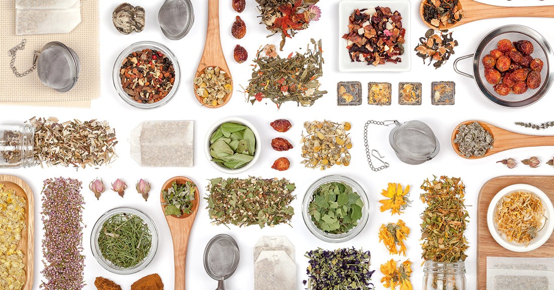 A diverse assortment of dried herbs, flowers, and teas laid out neatly against a white background, showcasing a variety of flavors and ingredients for brewing herbal infusions.