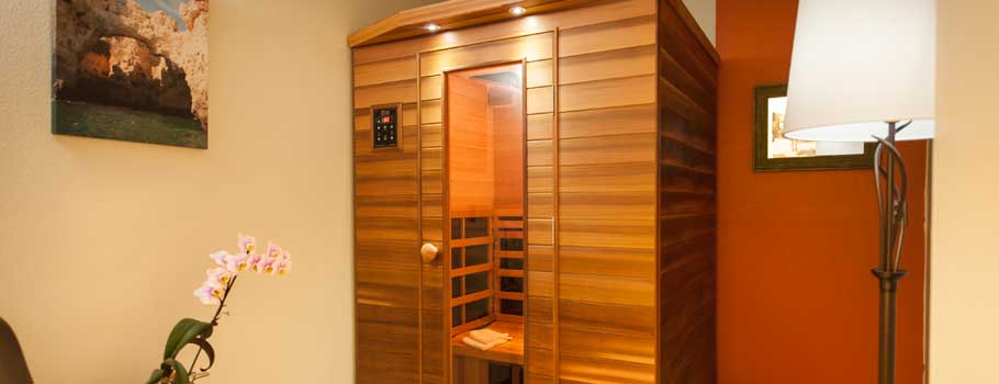 A tranquil wellness room featuring a modern wooden sauna, a floor lamp, and decorative touches like wall art and a potted orchid.