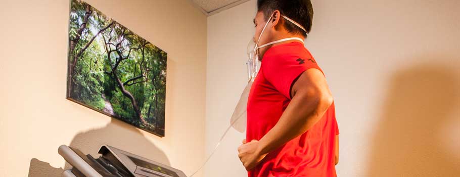 Man in red sports attire running on a treadmill while looking at a nature scene displayed on the wall.