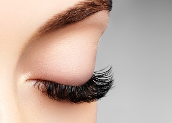 Close-up of a person's eye showcasing well-defined eyebrows, eyeshadow makeup, and long, curled eyelashes.