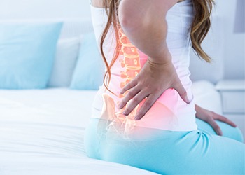 Woman experiencing lower back pain, depicted with an overlaid graphic highlighting the spine and pain areas.
