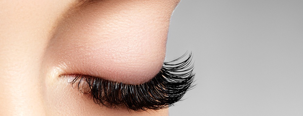 Close-up of a person's eye showcasing long, curled eyelashes against a neutral background.