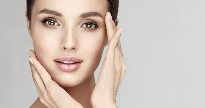 A woman with a radiant complexion gently touches her cheeks, showcasing her smooth, flawless skin against a neutral background.