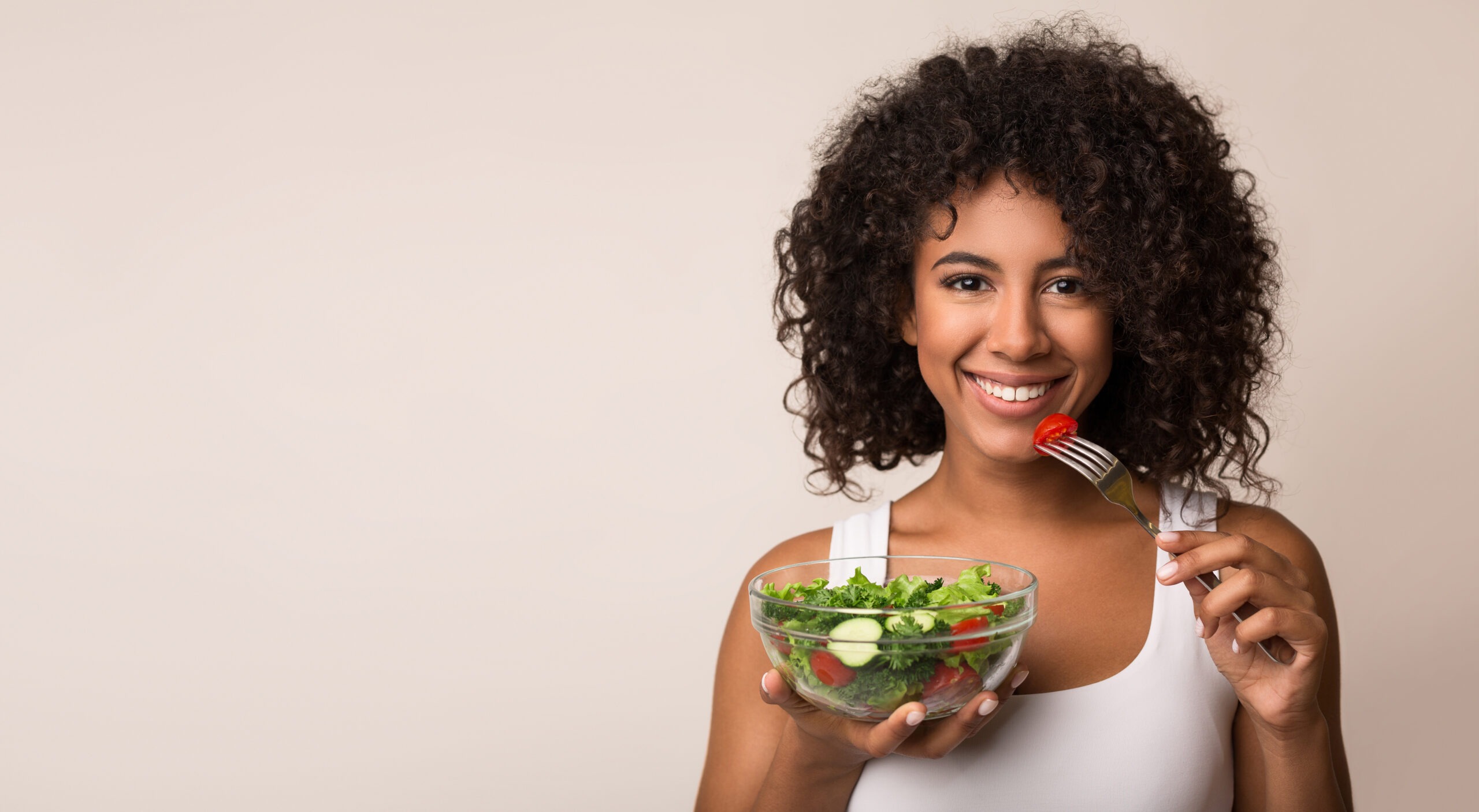 African-american woman eating vegetable salad over light background with copy space