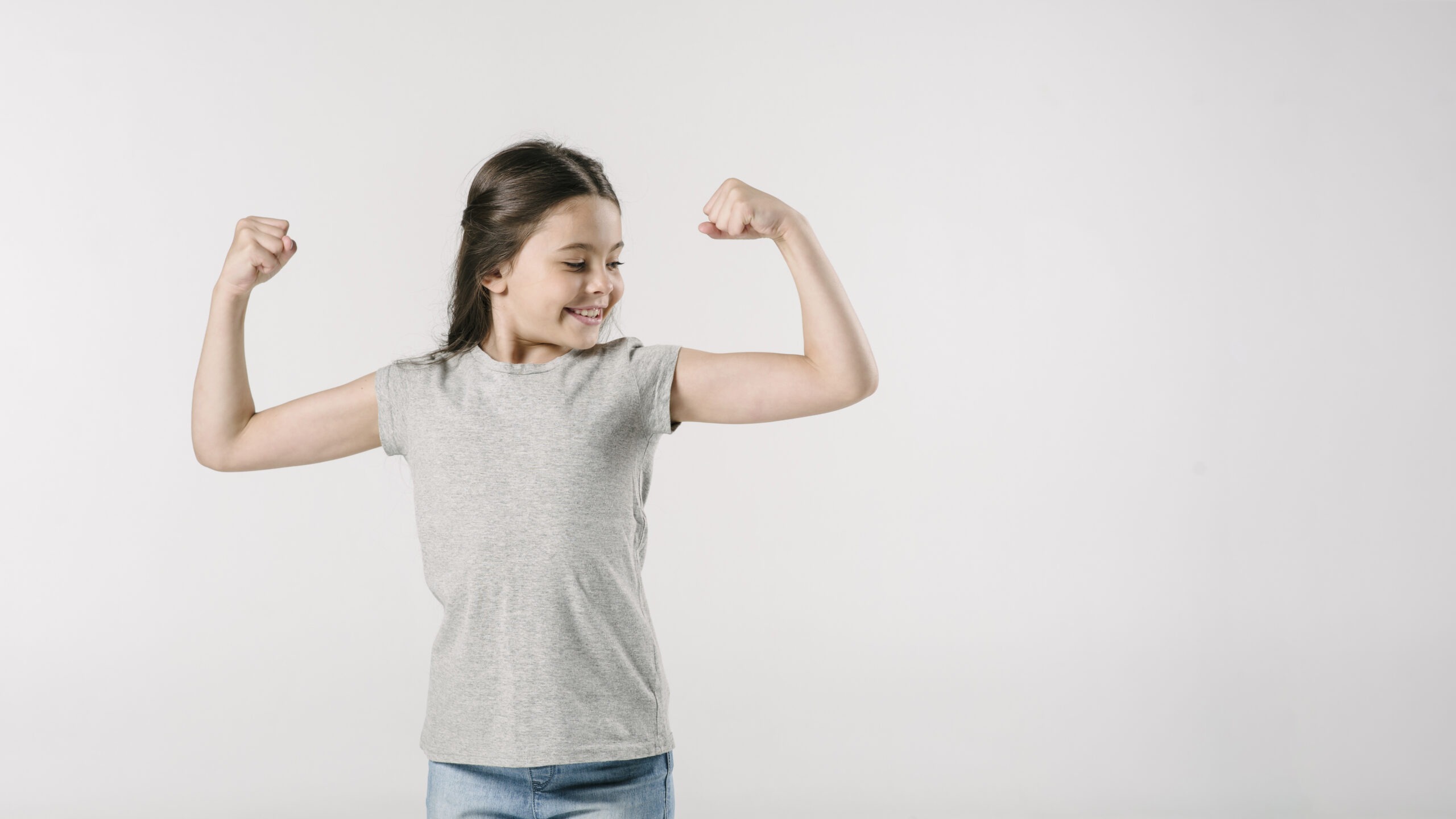 A confident young girl flexing her muscles with a proud smile, symbolizing strength and empowerment.