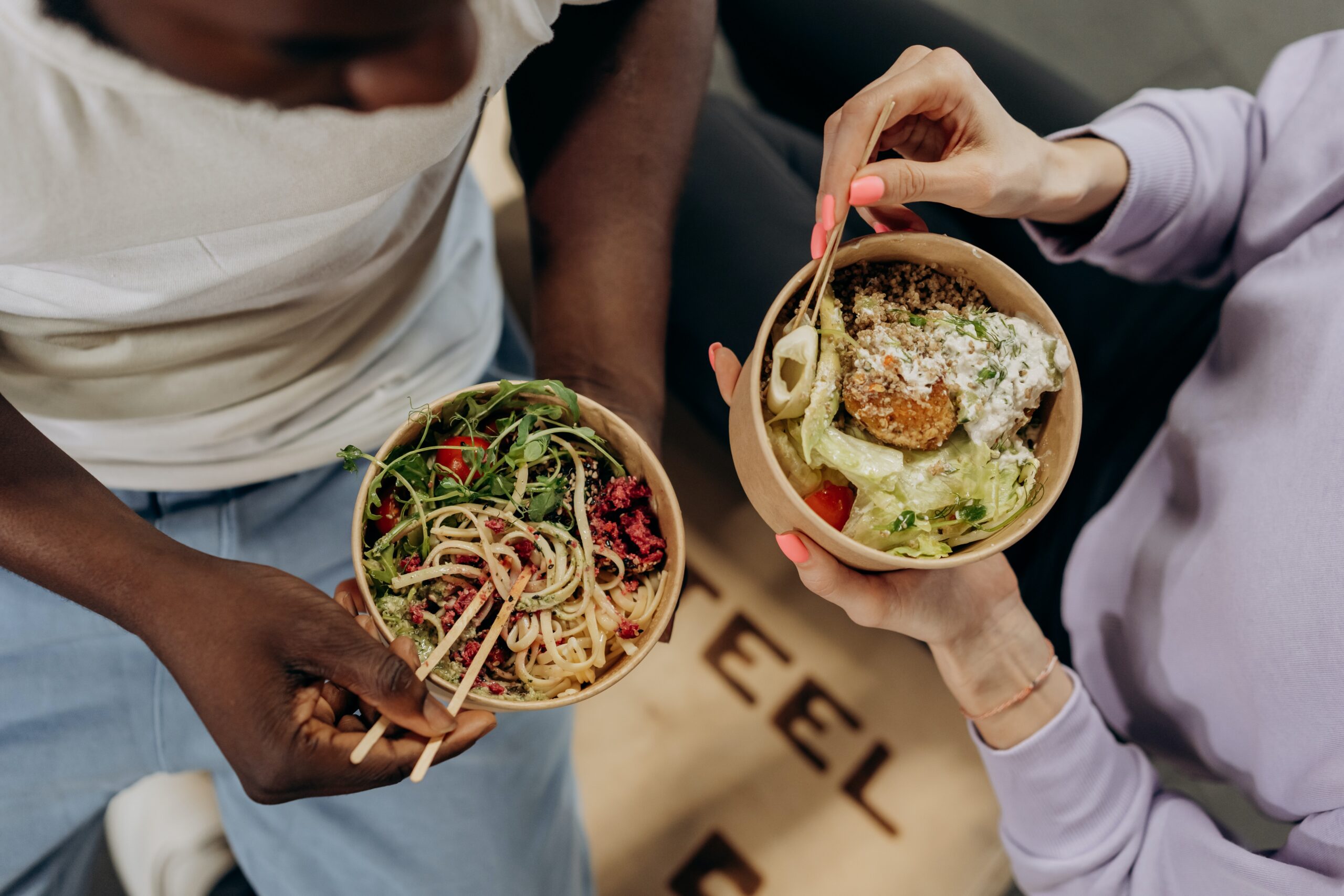 Two people sharing a casual meal, each holding a bowl filled with a healthy and colorful salad, enjoying a moment of connection over delicious-looking food.