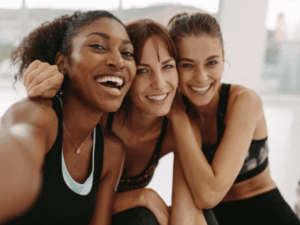 Three women smiling and taking a selfie together after a workout.