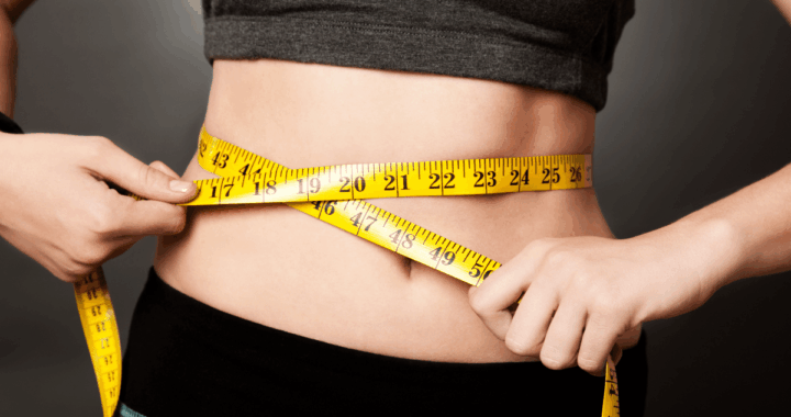 Person measuring their waist with a yellow tape measure around the abdomen.